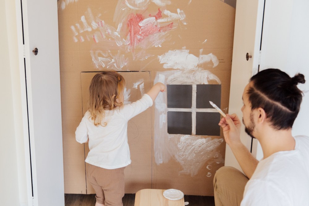 dad and daughter painting cardboard house during lockdown