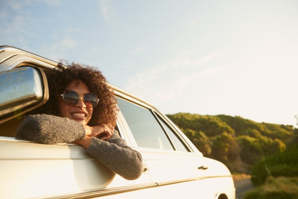 happy woman leaning out of the driving car on holiday