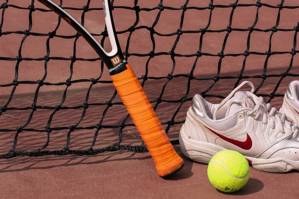racket and ball next to ladies tennis shoes