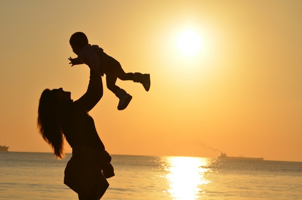 single mum holding young child in the air against sunset