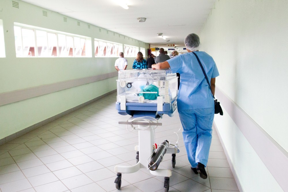 nurse walking away with premature baby in incubator