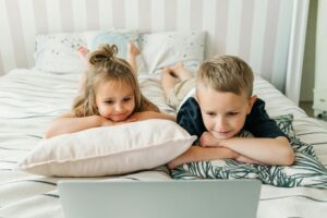 children watching film on laptop in bed