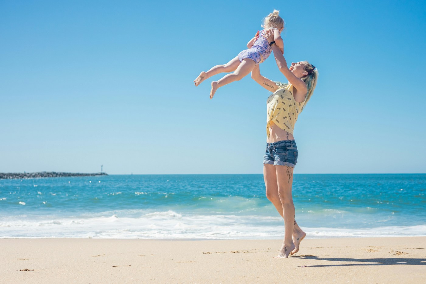 mum holding daughter up in the air on beach